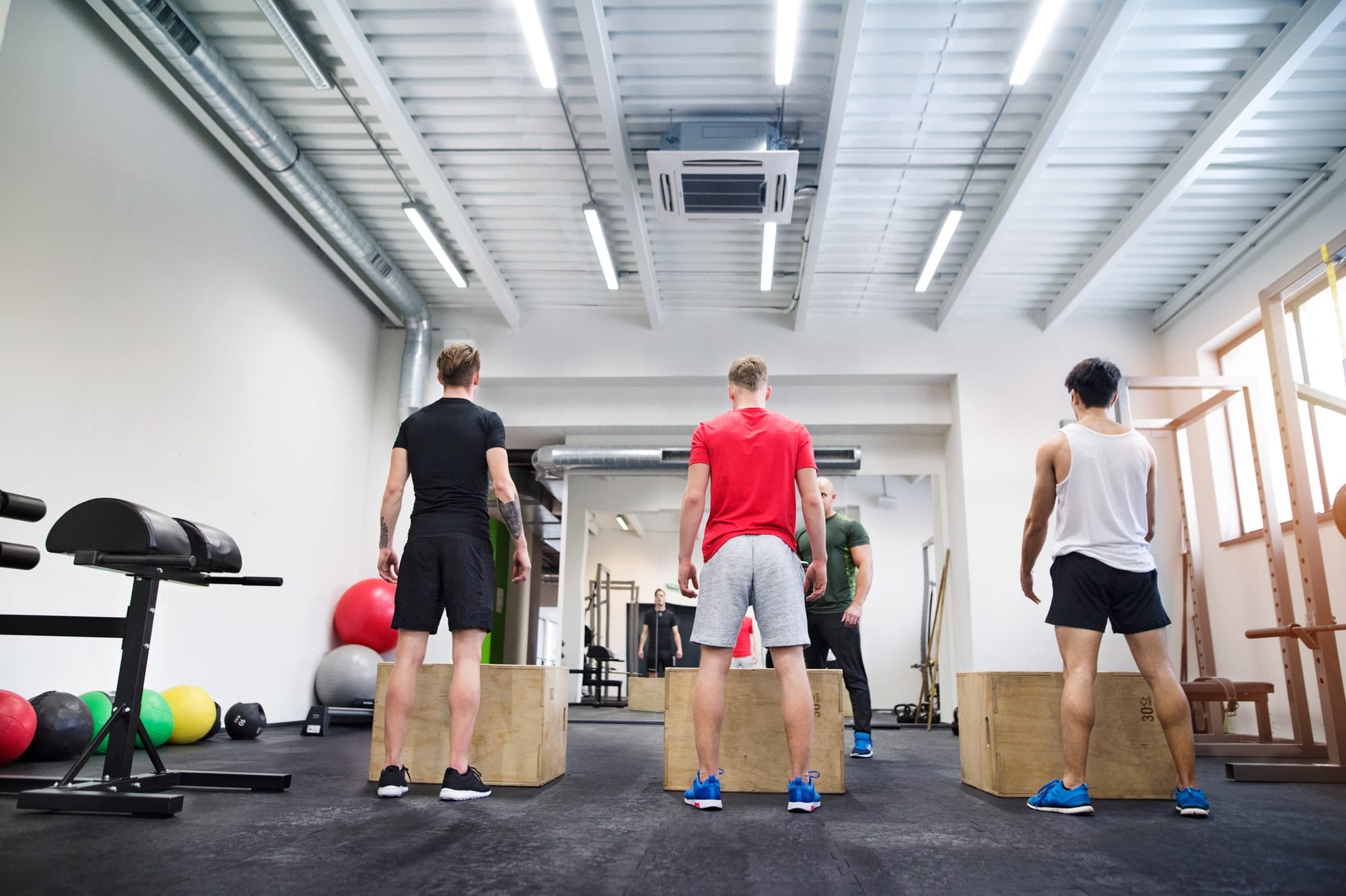 Men in gym with trainer exercising on fit boxes.